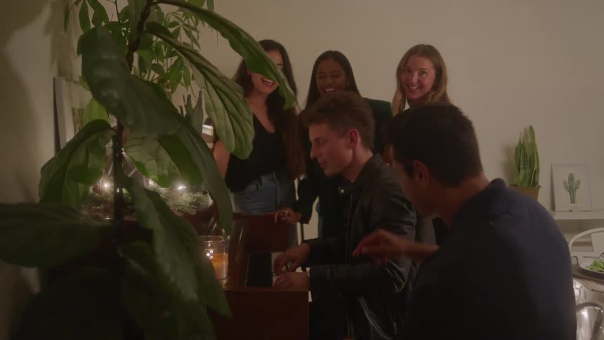 Friends gather around a piano singing with warm indoor lighting