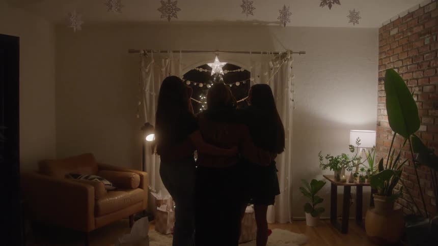 Based on the images from the video a group of three people are standing in a living room decorated with holiday lights they are silhouetted against a large brightly lit star that is hanging in a window