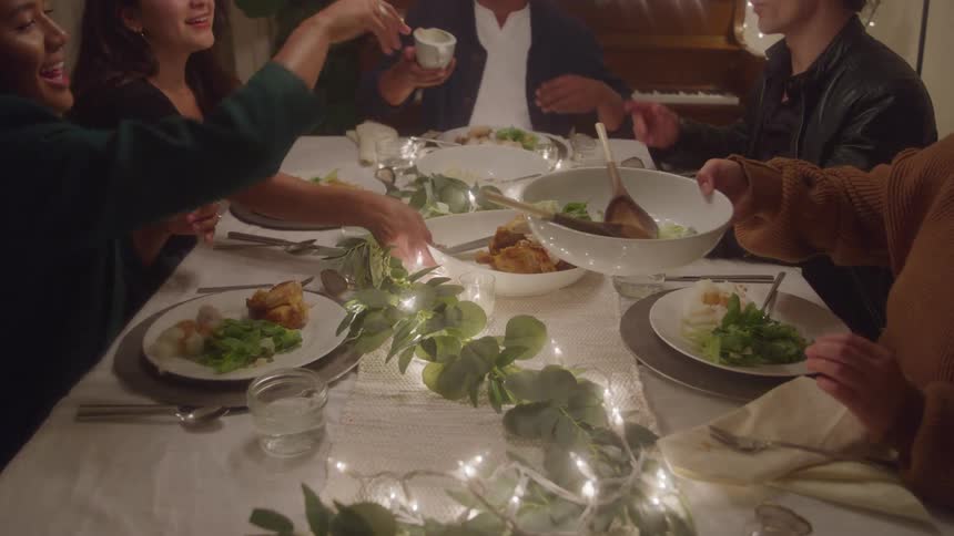 People share food at a table decorated with lights and greenery