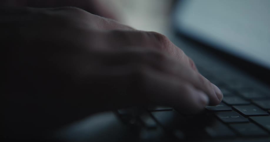 Hands type on a laptop keyboard in a dim setting