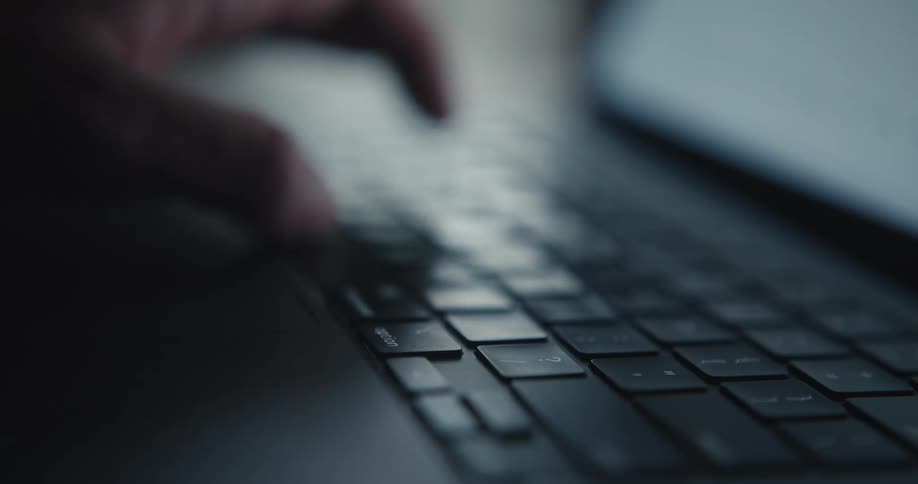 A hand types on a laptop keyboard in dim light