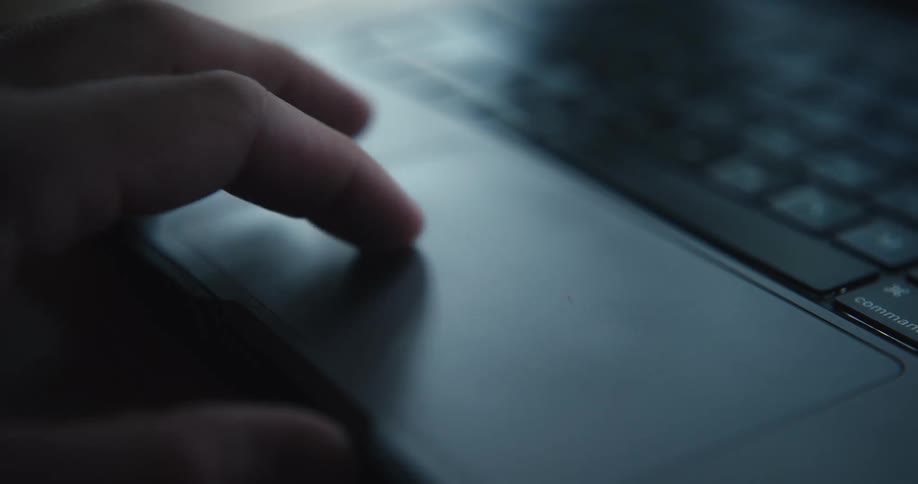 Person hand uses the touchpad of a laptop with part of the keyboard visible in the background