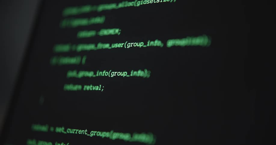 A close shallow focus view of a computer monitor shows green text and lines of code scrolling on a dark background