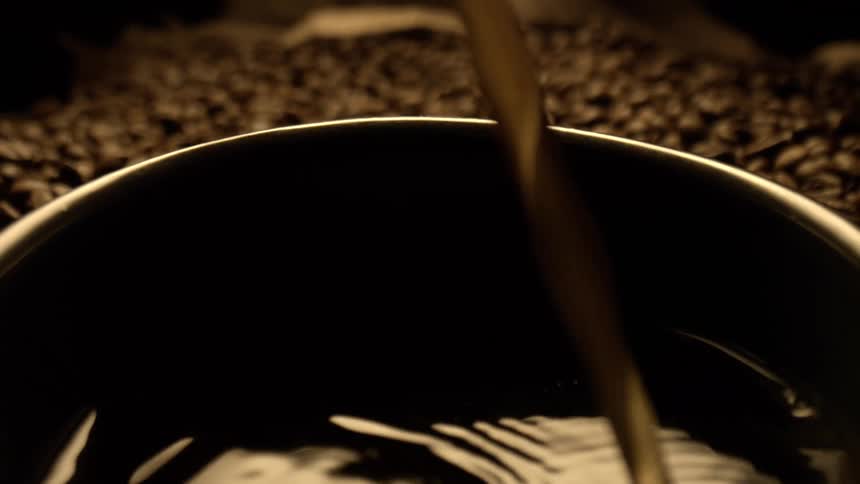 Coffee being poured into a cup with beans scattered in the background