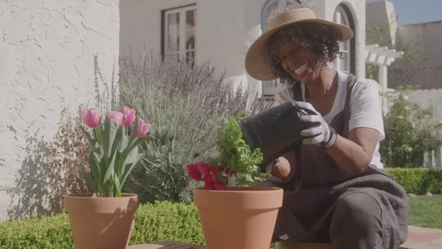 Smiling woman with a straw hat plants red flowers in a clay pot