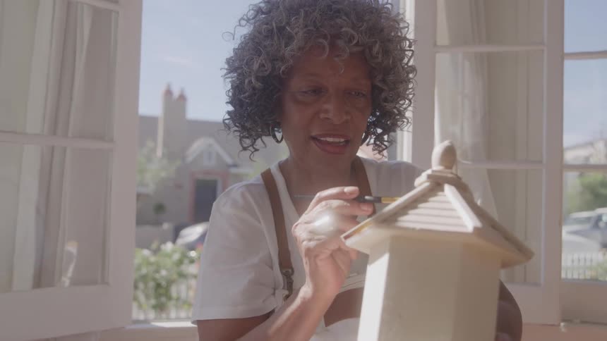 Woman handpaints a small wooden house