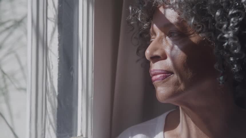 Based on the video a closeup shot shows a woman with curly hair looking out a window the light from the window illuminates her face and hair from the side