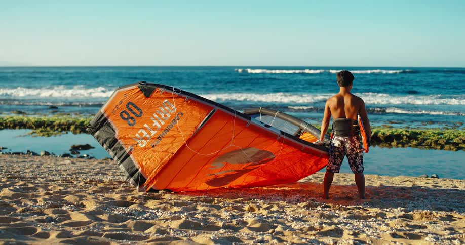 A man holds his kite surfing gear on the beach