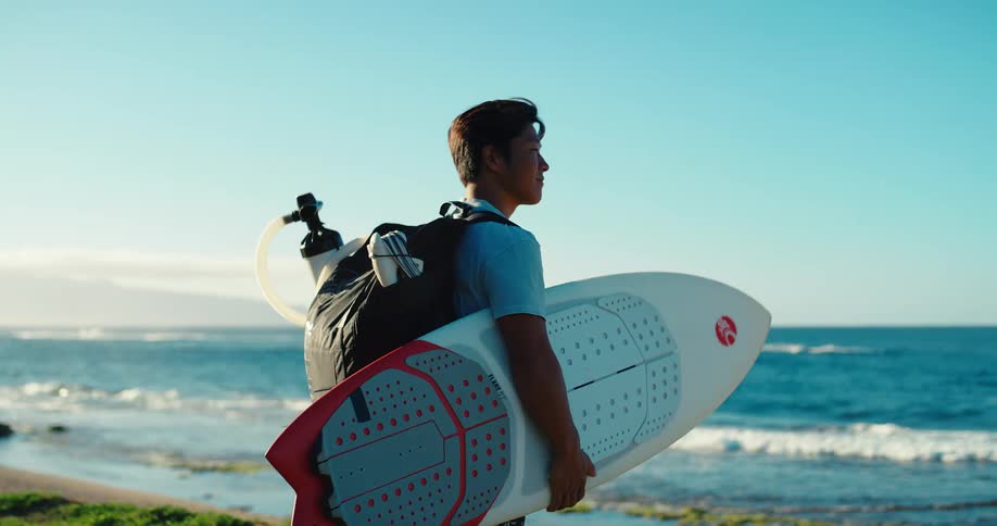 A young man carries a backpack of equipment for kite surfing