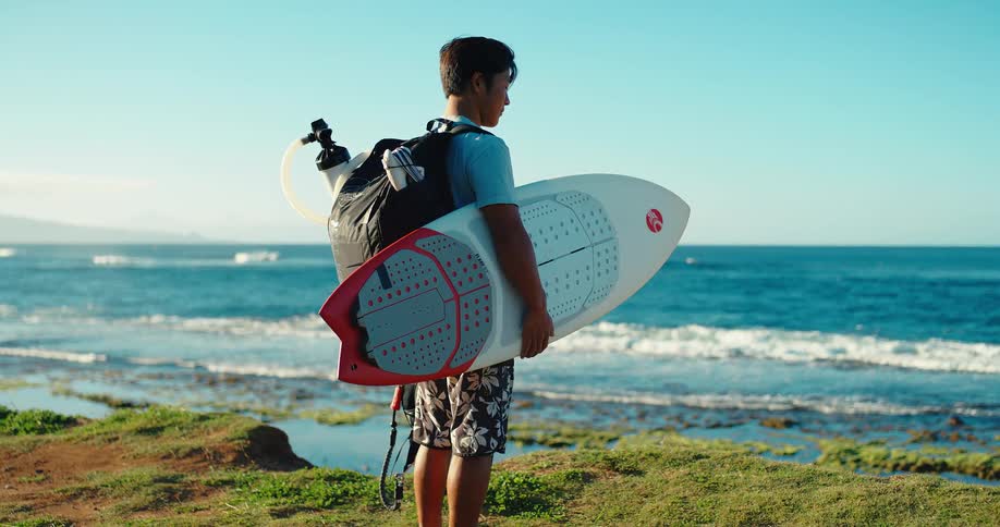 Surfer standing on the seaside grass holding a surfboard