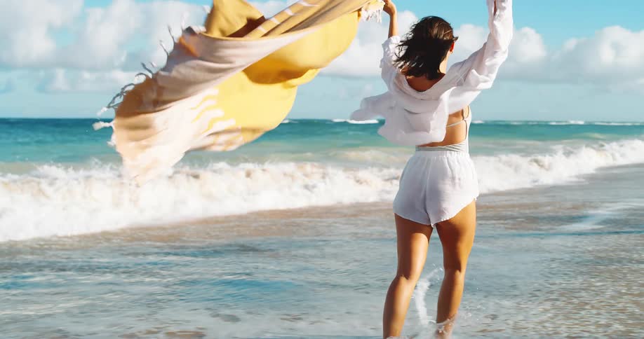 Person runs along the shoreline holding a flowing yellow scarf