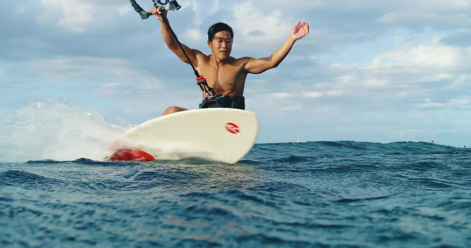 The video shows a man kiteboarding on the ocean he is standing on a board and holding onto a bar and as the kite pulls him forward he uses his momentum to jump out of the water