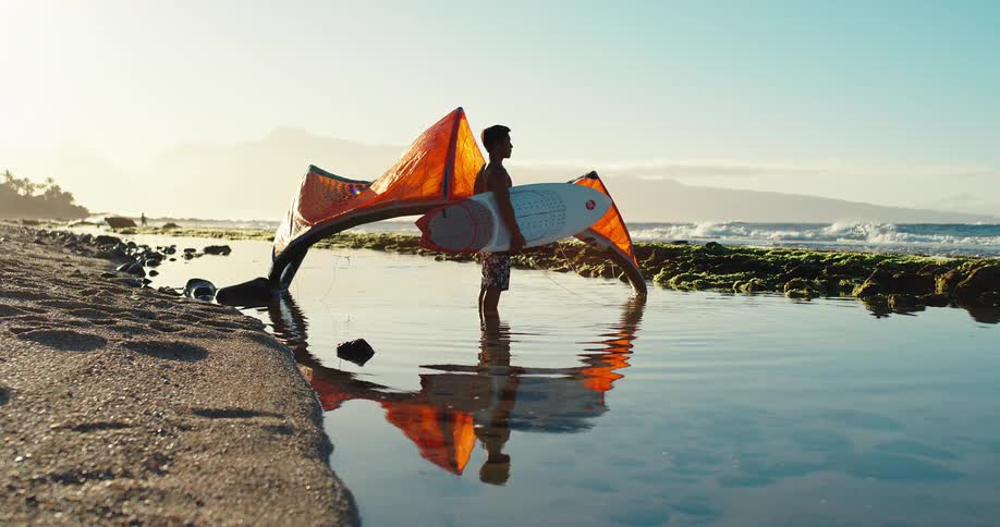 A man is standing in the water with his kite surfing gear