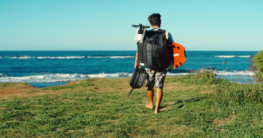Man carrying a surfing equipment walks along the shoreline
