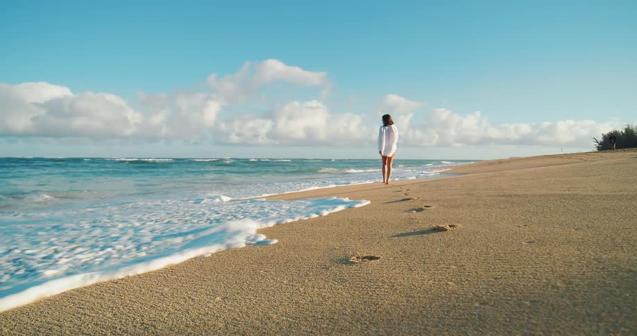 Woman walks alone along the shoreline leaving footprints in the sand