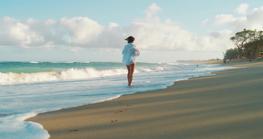 Woman walks along the shoreline with her feet in the water