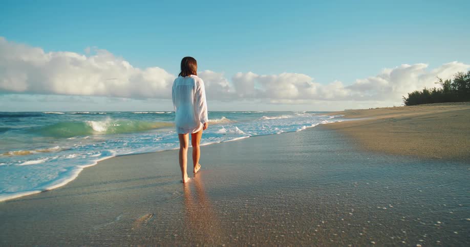 Woman walks barefoot on wet sand near the ocean waves