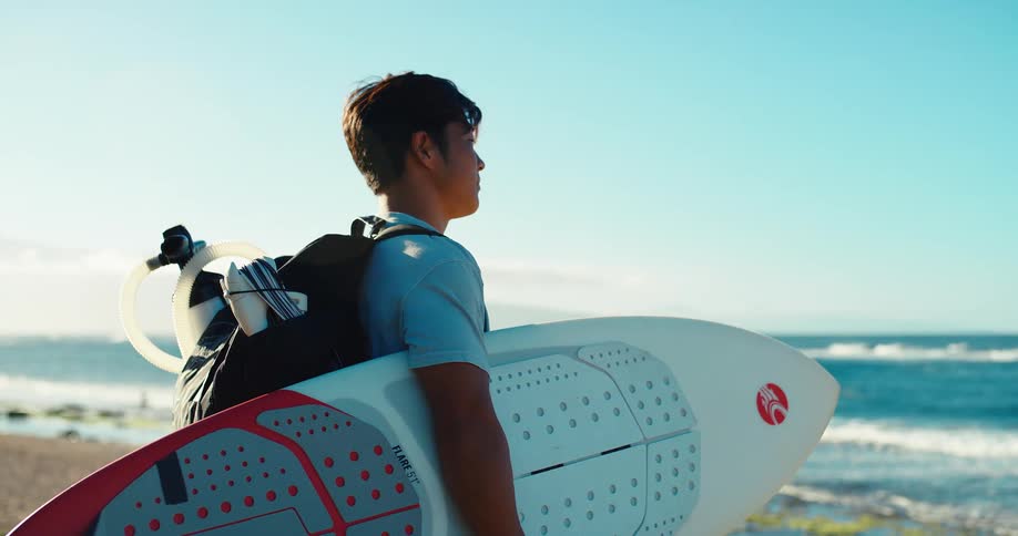 The man holds his kite surfing gear and looks out over the ocean