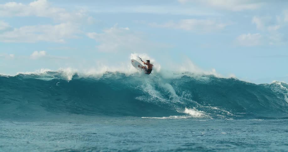 An adventurous man is kite surfing over tall ocean waves
