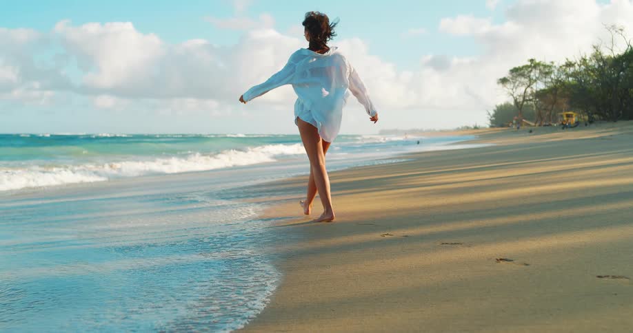 Woman walking barefoot across the beach as waves roll into shore