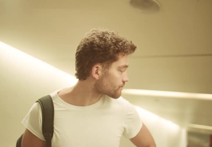 Based on the video a man is playing an acoustic guitar indoors with light streaming in from a window he is seated and has a plant on the table next to him