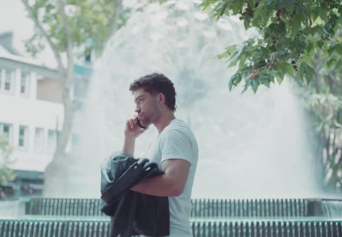 A man takes a seat near a water fountain while hes talking on the phone