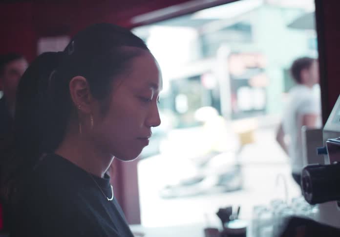 Female barista works the coffee machine while a customer waits on the sidewalk outside