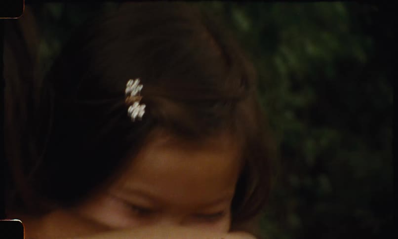 The video shows a young girl with long brown hair resting her head on her arm with a serious and contemplative expression she has two small white flowershaped hair clips in her hair