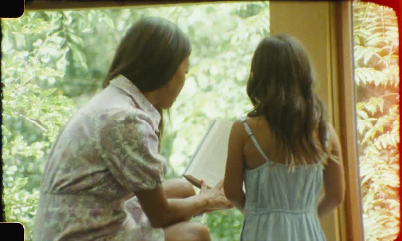 Woman sitting next to a girl showing a book near the window