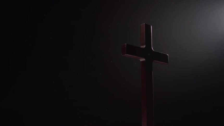 A wooden cross stands against a dark setting