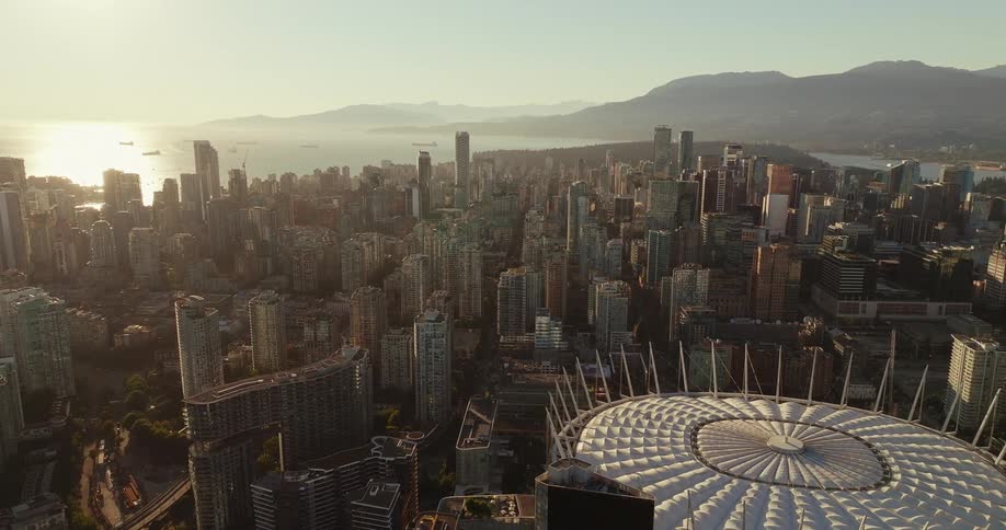 Drone view of a sunlit city skyline with a domed stadium