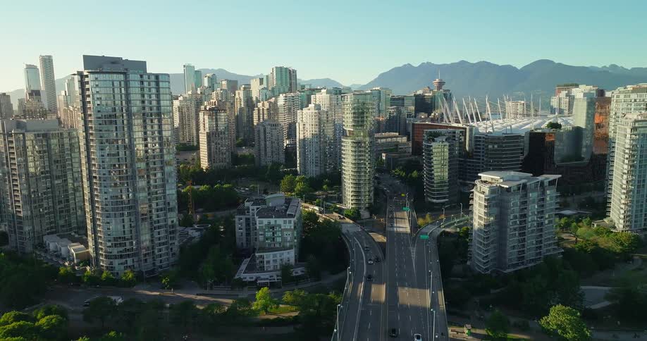 An aerial view of a busy coastal city shows a skyline of tall modern residential and commercial buildings under a clear blue sky