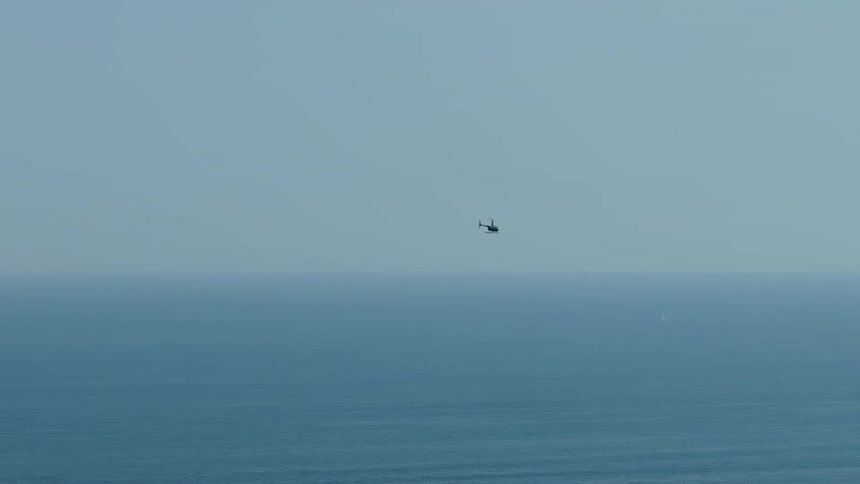 Boats sail on the water as a helicopter flies overhead