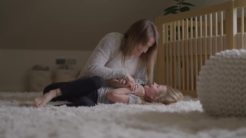 A mother tickles her daughter as she laughs