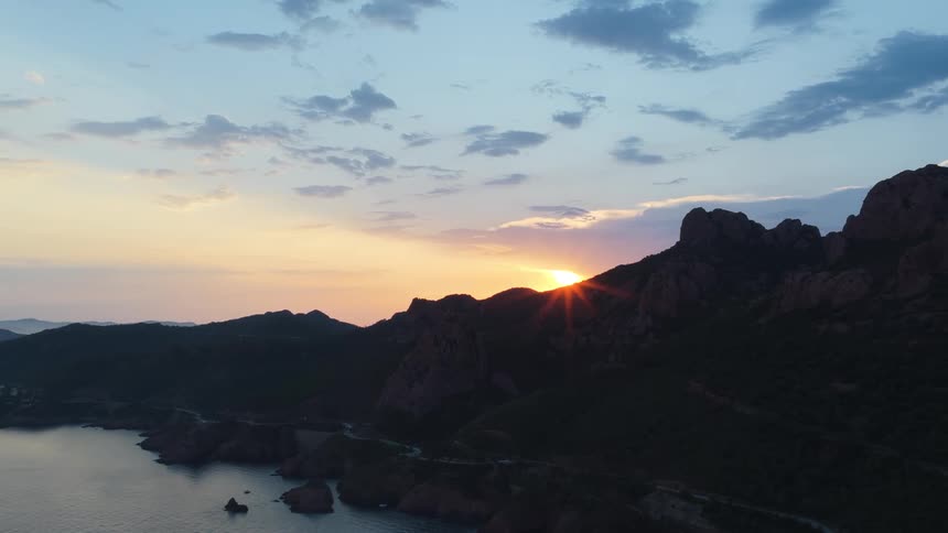 Setting sun glows on the horizon over mountains along the coast