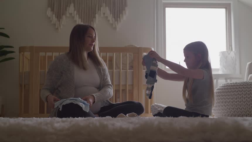 Pregnant mother and daughter sitting on the floor organizing baby clothes