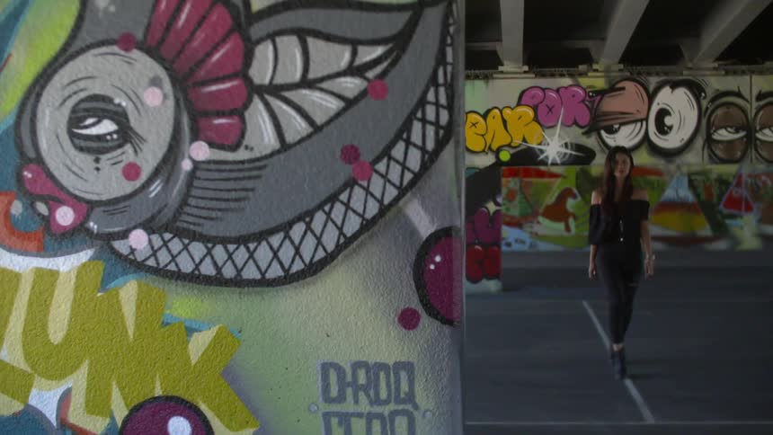A woman walks on a straight white line in a parking garage with graffiti covering walls and columns