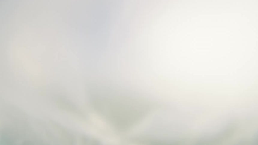 Looking straight up at a clear blue sky with a bright sun on the right a sheer white piece of cottonlike fabric moves around and over blocking out most of the sky but allowing in some light from the sun