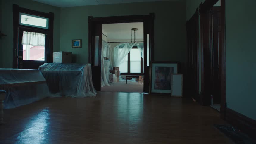 An empty old room with shiny wooden floors partially covered in plastic sheeting