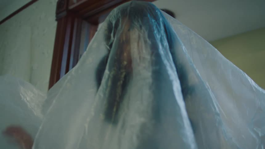 Person covered by a large translucent plastic sheet inside a room