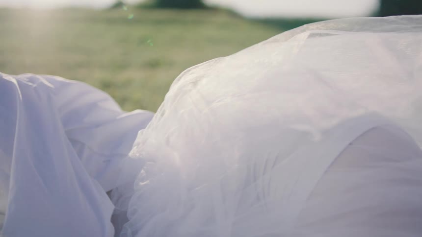 A view from a low angle shows a woman lying on a grassy hill with her head resting wearing a white dress