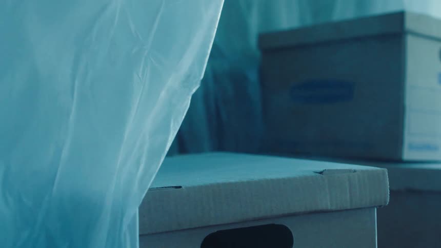 Cardboard moving boxes sit under draped plastic in a room