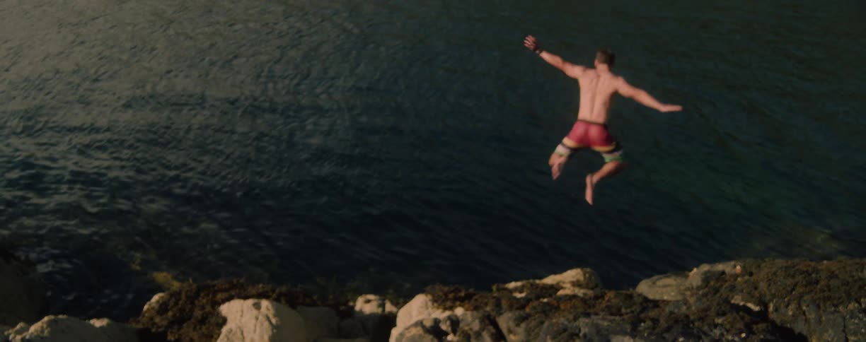 Man in red shorts jumps off a cliff into the sea