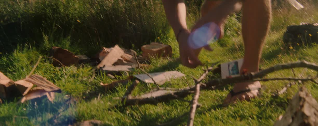 A man hurriedly leans over and picks up some branches from the ground