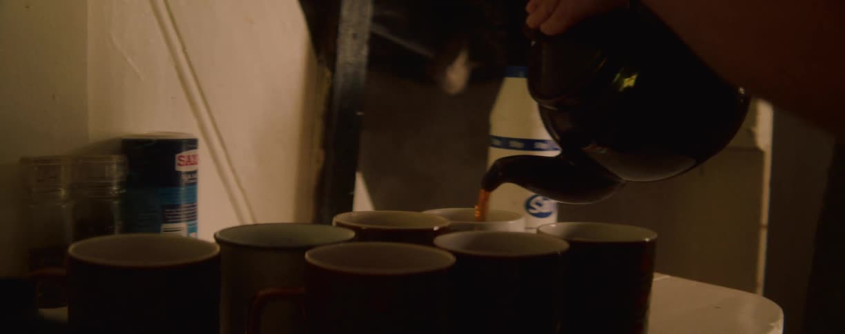 Coffee being poured into several mugs lined up on the table