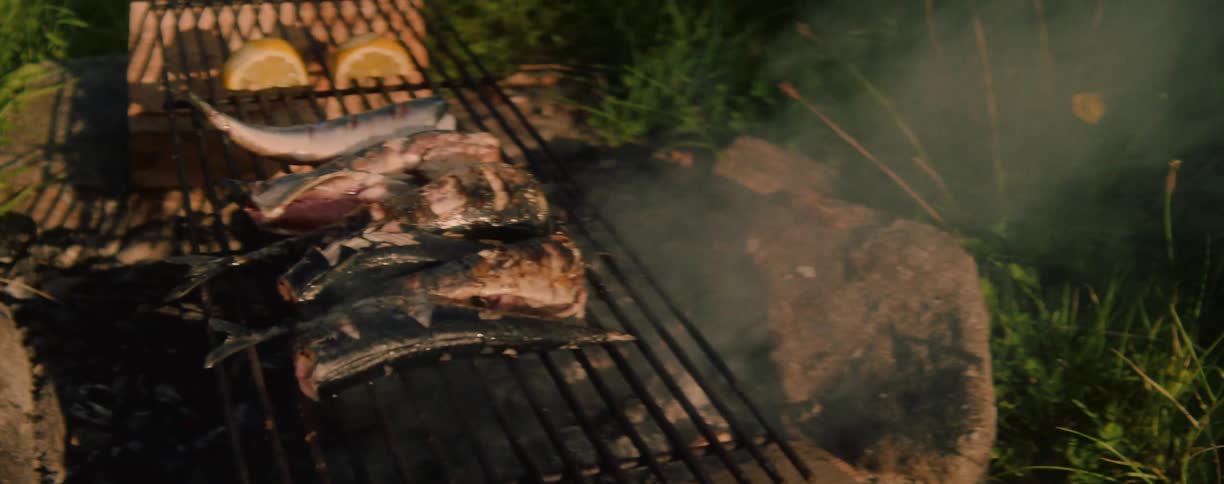 Fish grilling with lemon slices over a barbecue outdoors