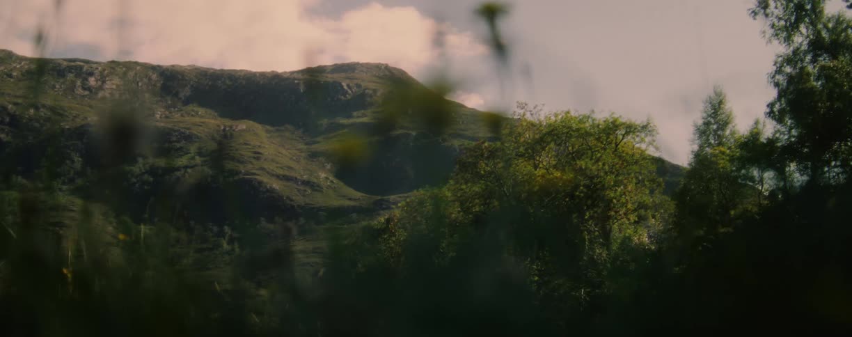 A majestic green mountain landscape under a dynamic cloudy sky with dense vegetation in the valley and on the slopes