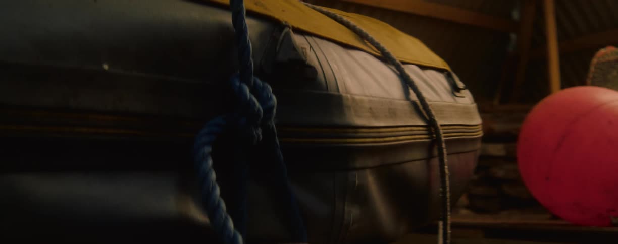 A close angled view shows the side of packed inflatable boat with a yellow cover with a thick blue rope tied to it and a red buoy nearby