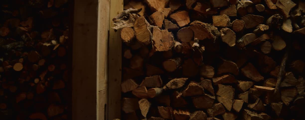 A view of a large stack of firewood shows logs with a variety of light and dark brown textures