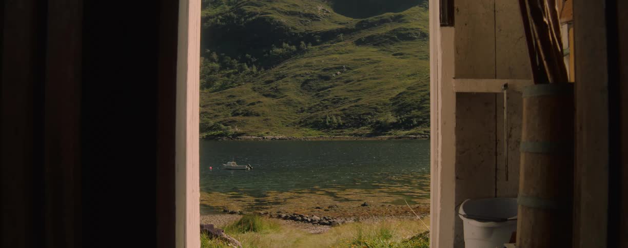 A serene view of a lake and green hillside seen from the doorway